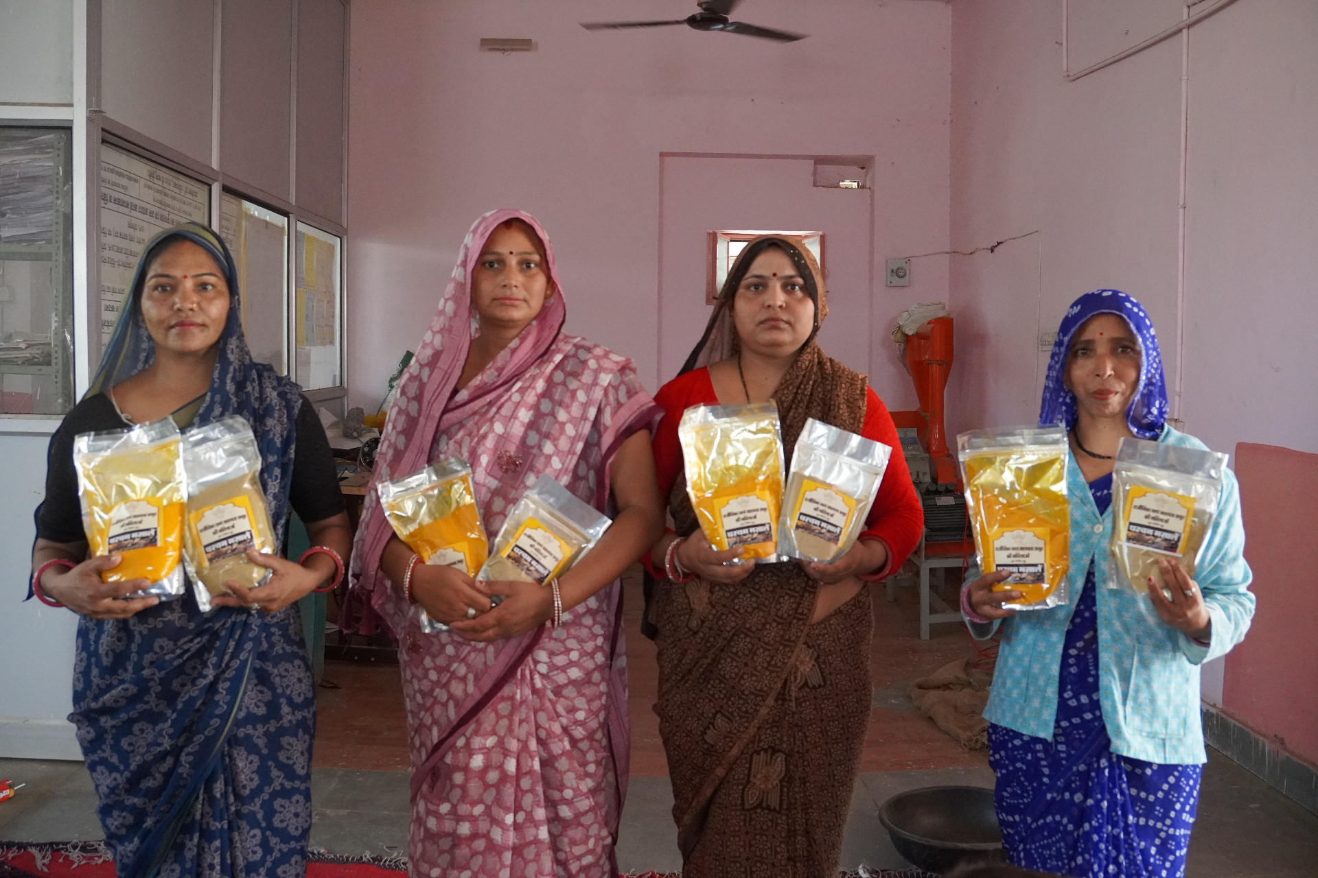 Four women producers from a Rajeevika enterprise in Rajasthan holding packets of turmeric and besan they have milled and packaged themselves.