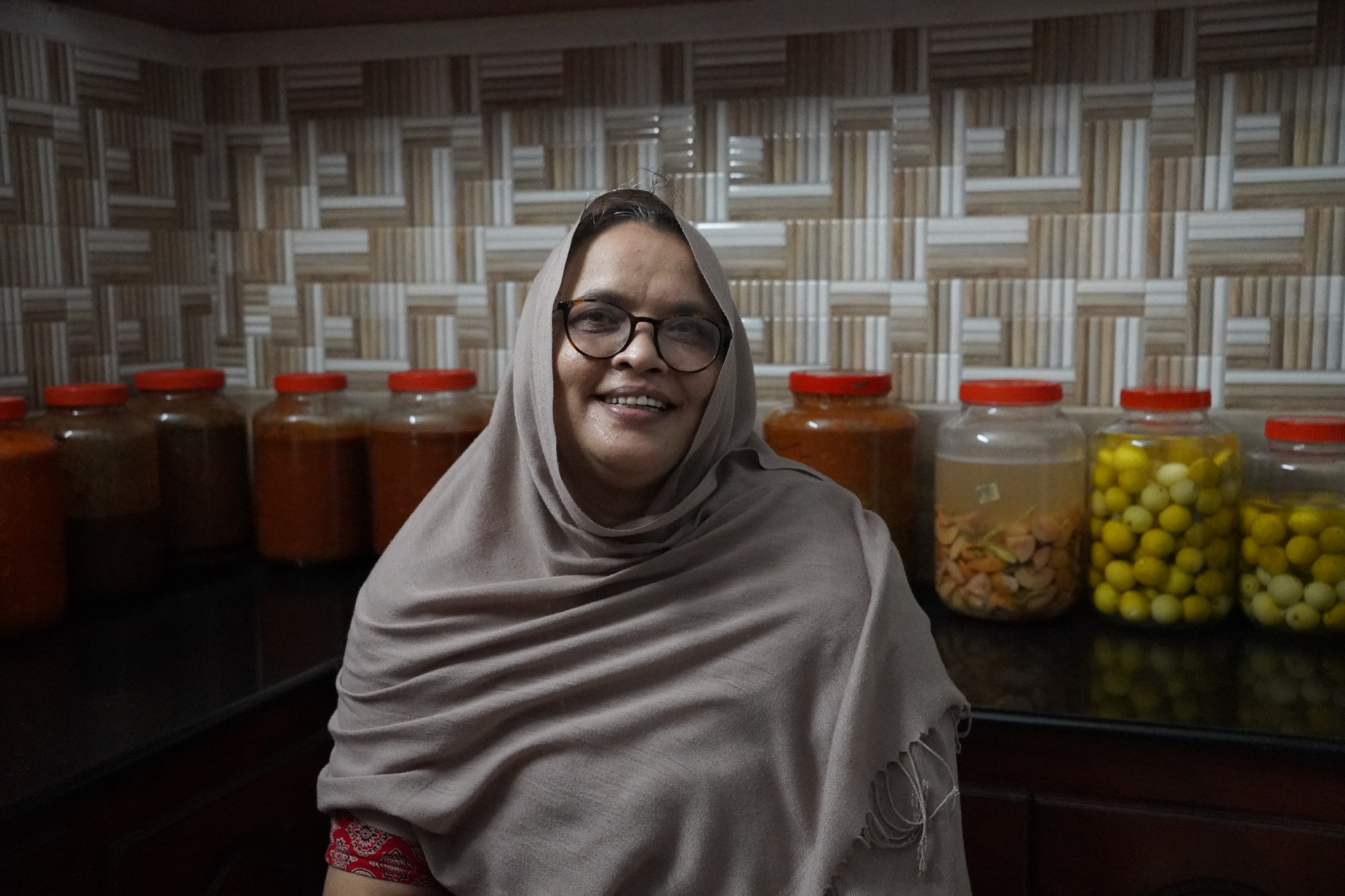 A woman pickle producer in Rajasthan seated in front of large jars of pickle in her storage room.