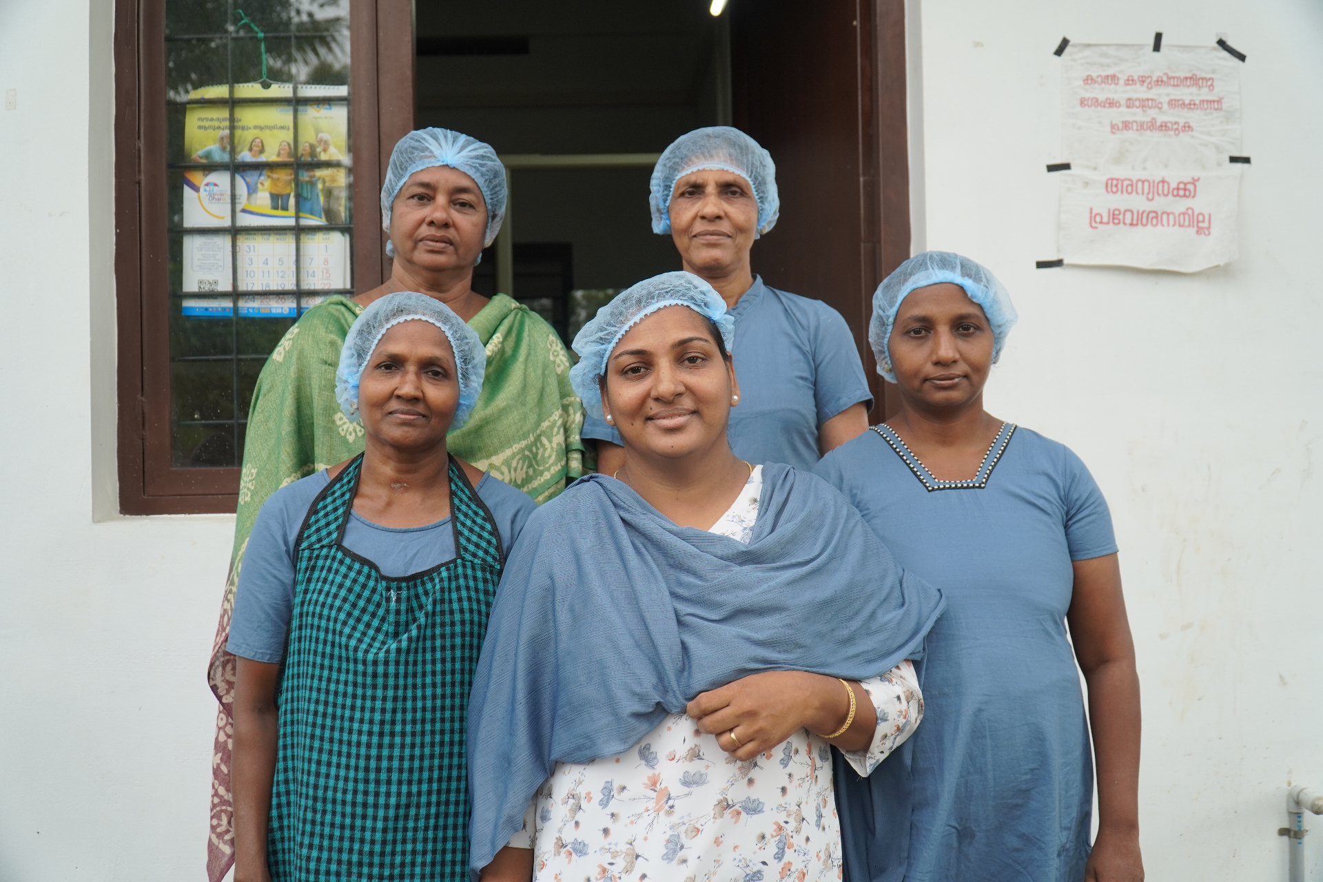 Five members of the Kairali Amrutham Nutrimix unit at the entrance of their workshop in hairnets.